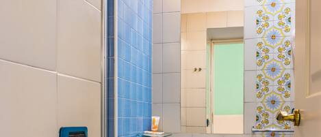Une salle de bain avec des carreaux bleus, un lavabo blanc, un miroir et une douche.
