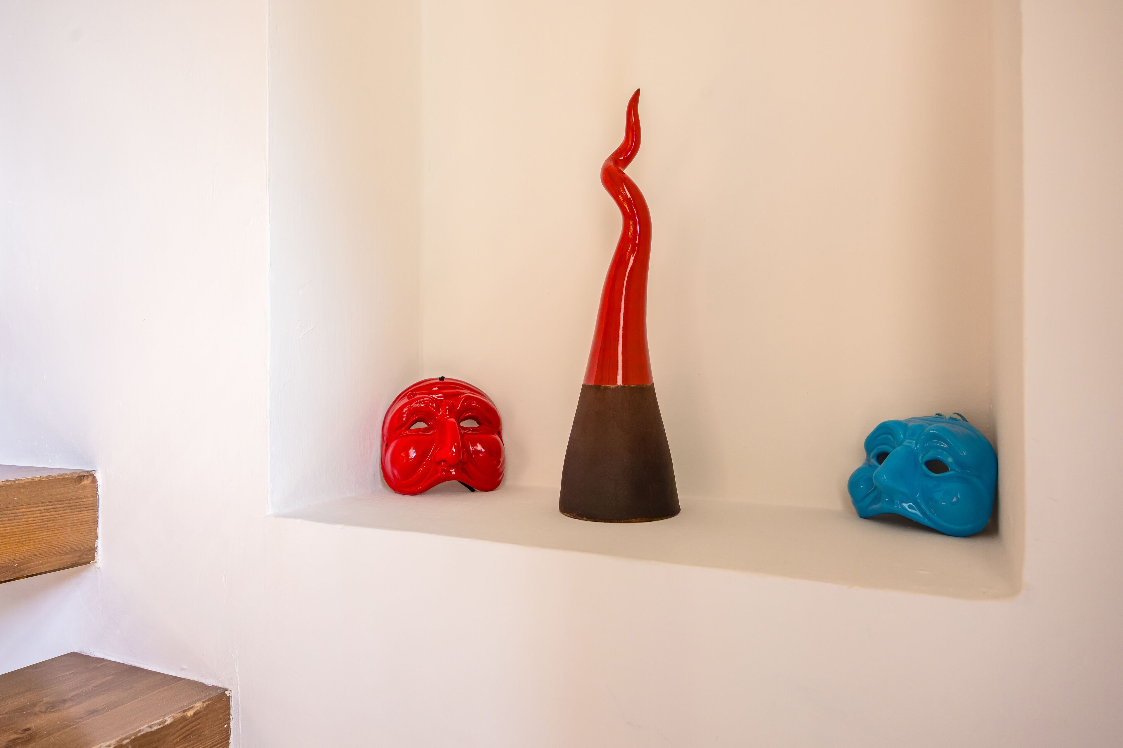 Three ceramic masks on a white shelf against a wall.