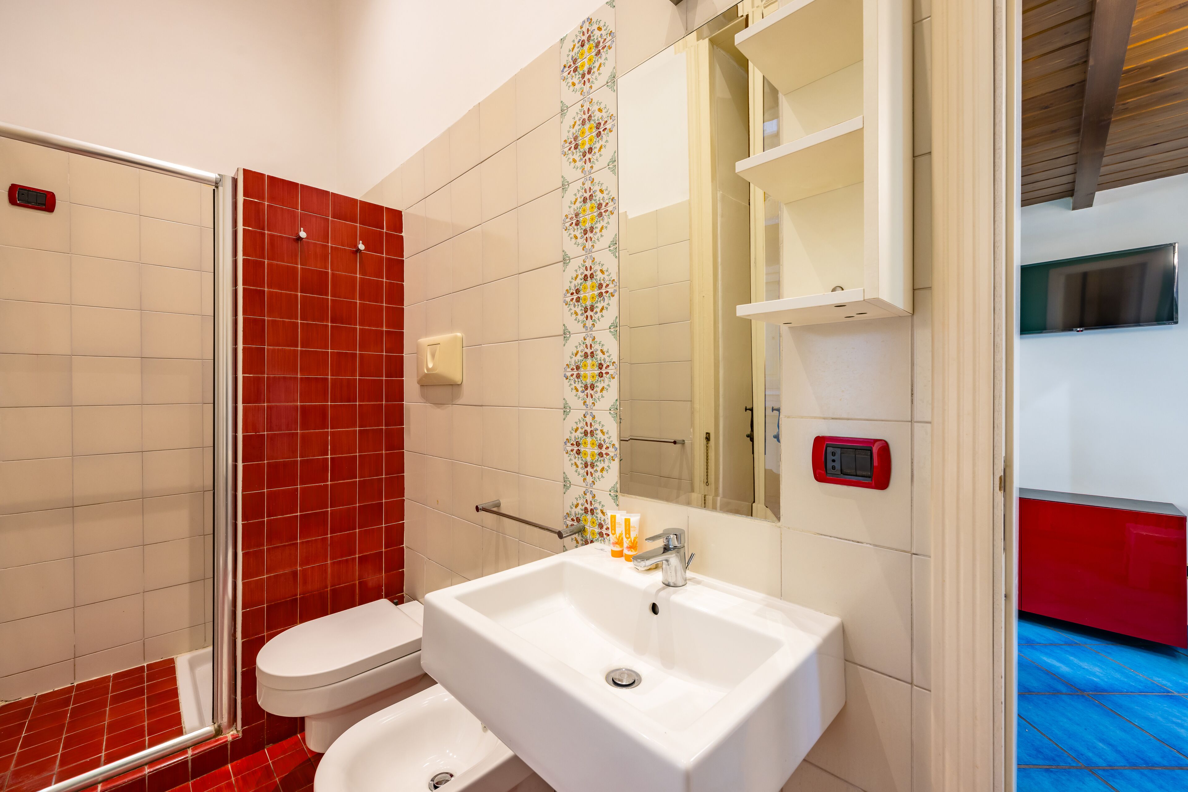 Ein Badezimmer mit weißem Waschbecken, einer roten Duschkabine und einem Spiegel über dem Waschbecken.