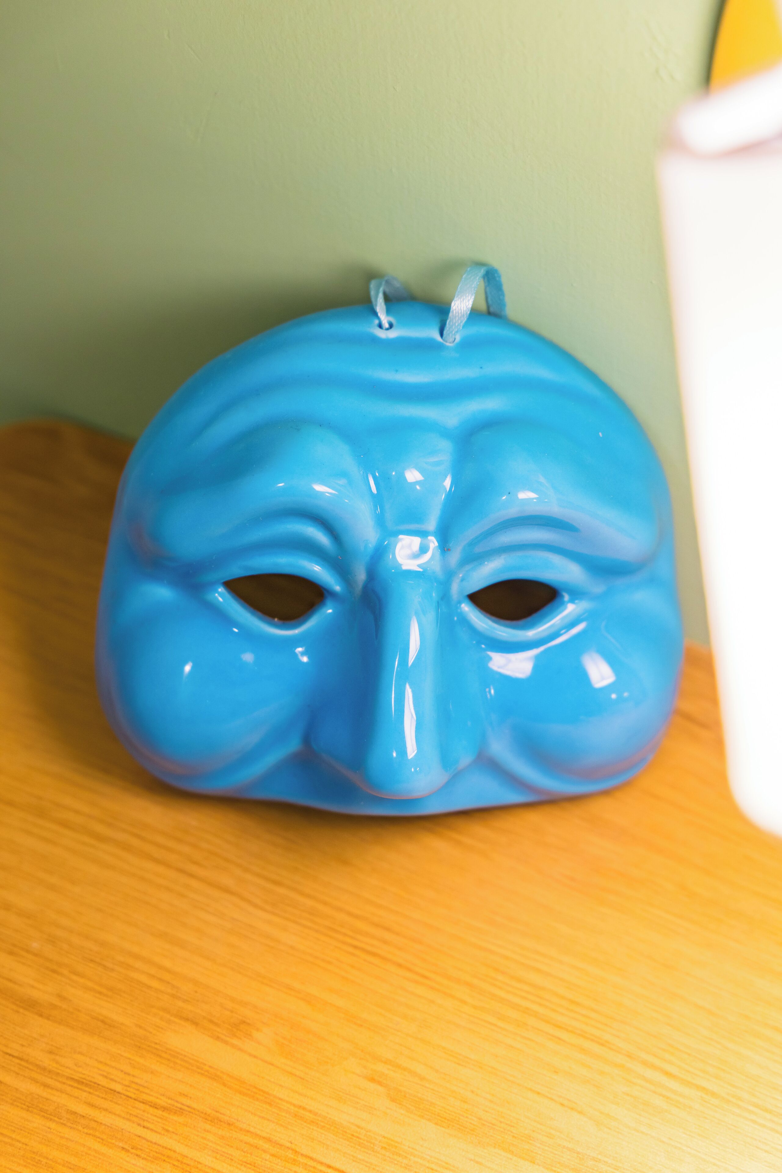 A blue ceramic mask with a handle on a wooden surface.
