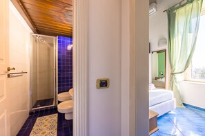 A bathroom with a shower, toilet, and a bed with a window.