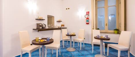 A dining area with white chairs and round tables, blue tiled floor, and a window with frosted glass.