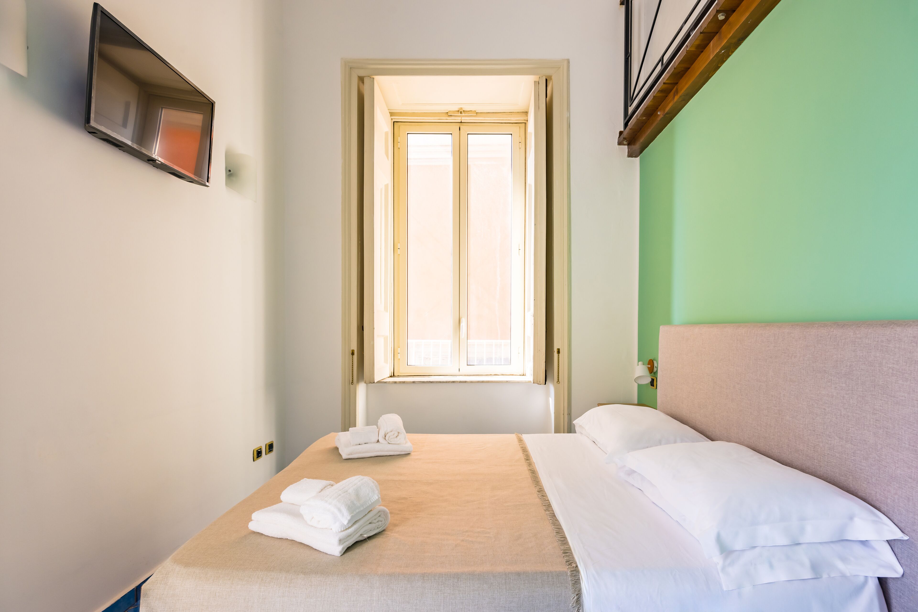 Une chambre d’hôtel équipée d’un lit, d’une fenêtre et d’un téléviseur à écran plat fixé au mur.
