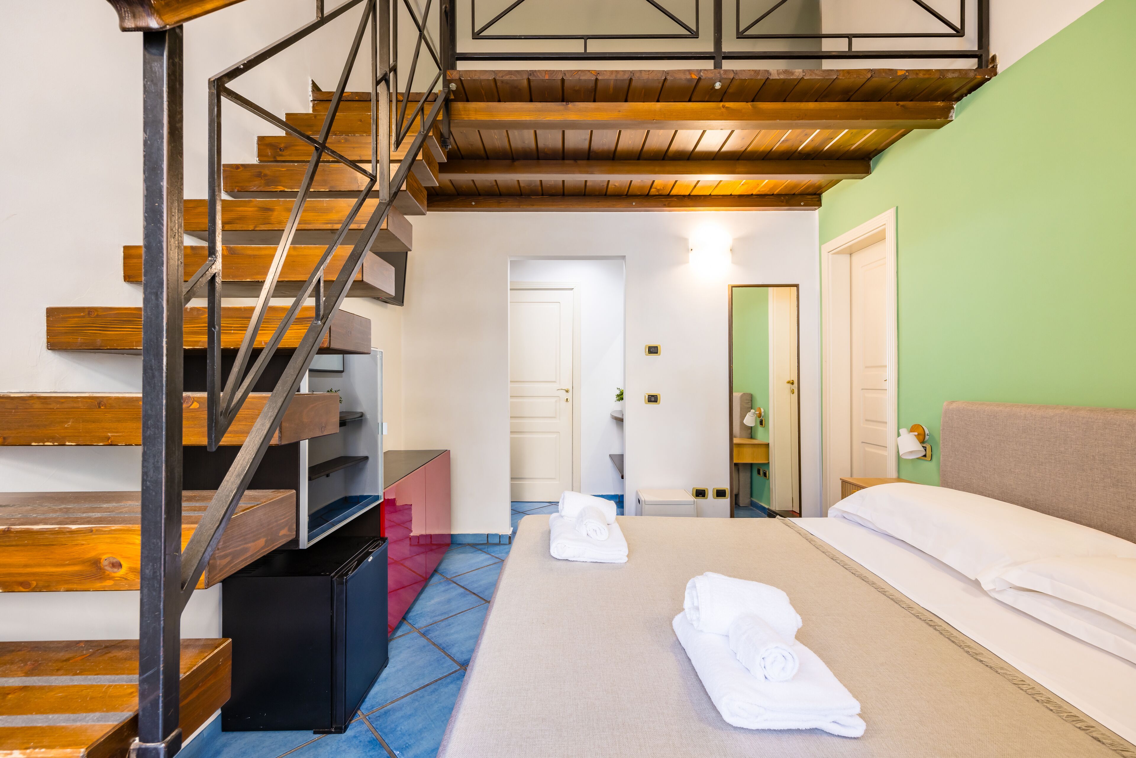 A hotel room with a wooden staircase, a bed with white linens, and a bathroom with a green wall.
