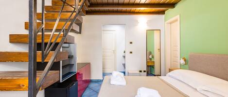 A hotel room with a wooden staircase, a bed with white linens, and a bathroom with a green wall.