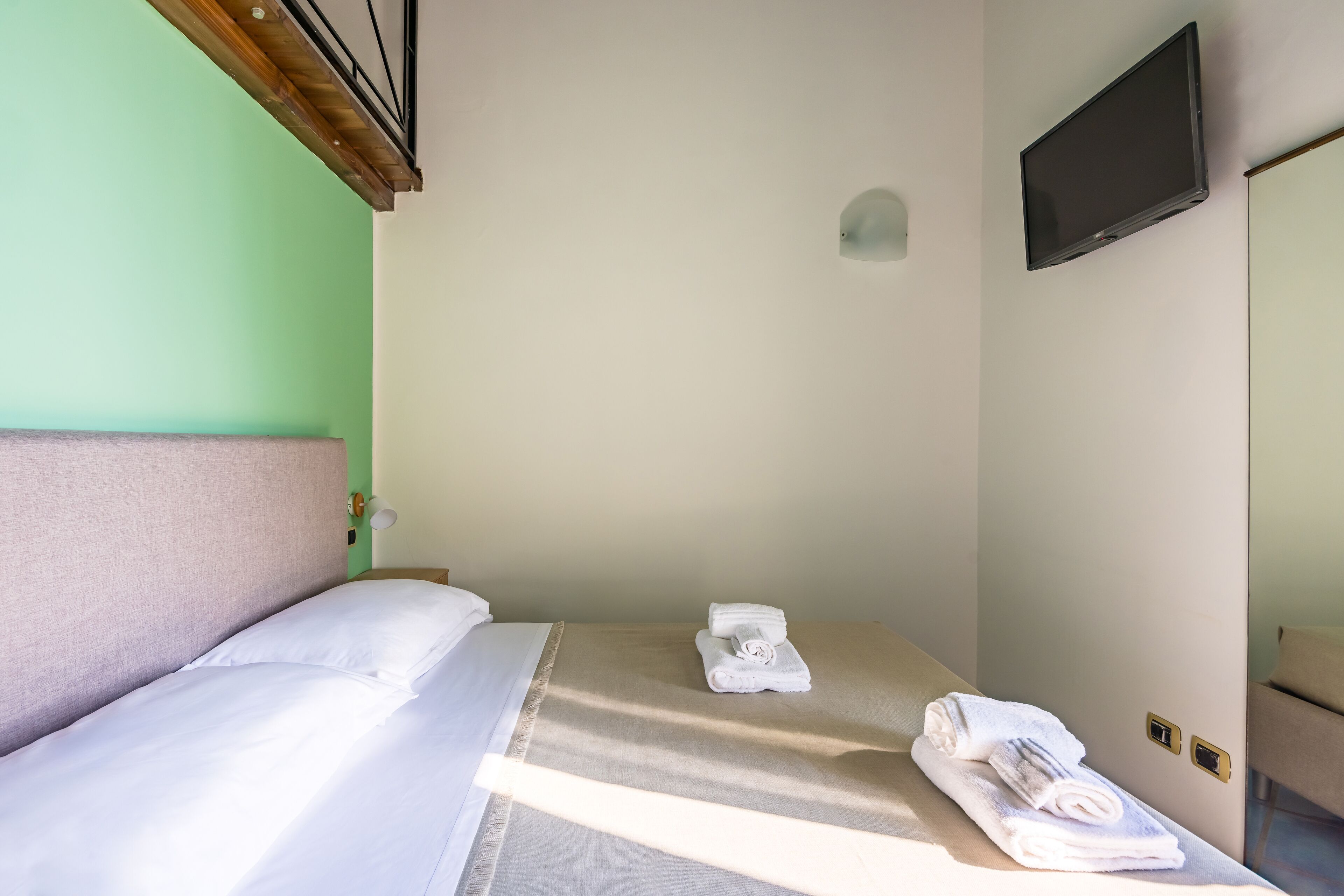Une chambre d’hôtel avec un lit, un téléviseur fixé au mur et une petite table avec des serviettes.