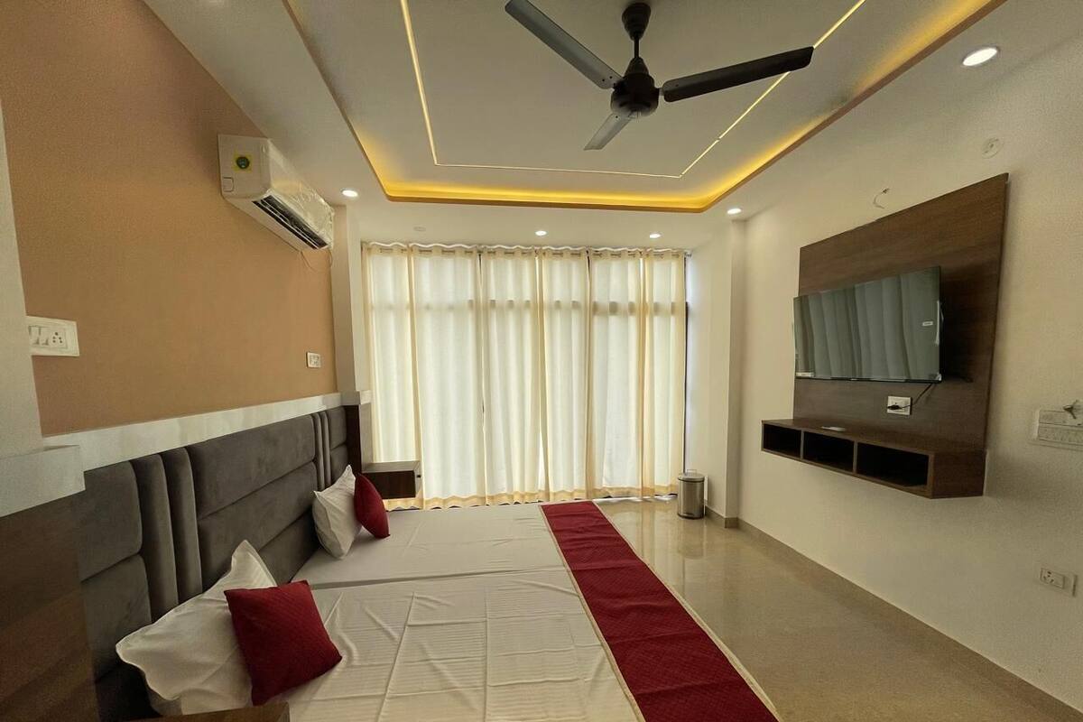 A modern hotel room with a large bed, a ceiling fan, an air conditioning unit, a TV mounted on the wall, and a window with curtains.