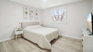 Ein Schlafzimmer mit Bett, Nachttischen, einem Fenster und Wandbildern.