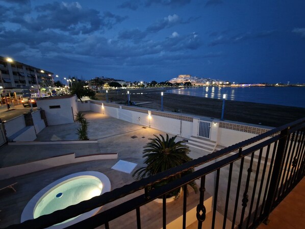 A balcony with a pool, a view of the sea, and a cityscape in the background.