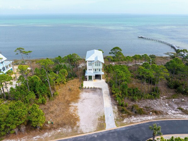 Une maison à deux étages dotée d’un grand porche, entourée d’une forêt dense de pins et offrant une vue sur l’océan.