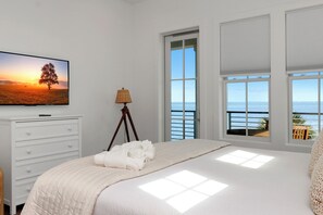 Une chambre à coucher avec un lit, une télévision, une lampe et une fenêtre donnant sur la mer.
