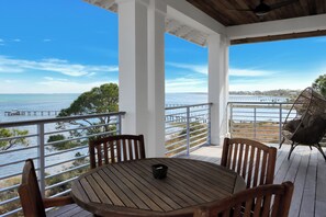 Une terrasse en bois avec une table et des chaises, donnant sur une étendue d’eau et une jetée.