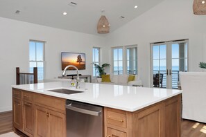 A spacious kitchen with a large island, wooden cabinets, and a view of the ocean through large windows.