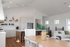 A spacious kitchen with white cabinetry, a wooden dining table, and a seating area with a white sofa.