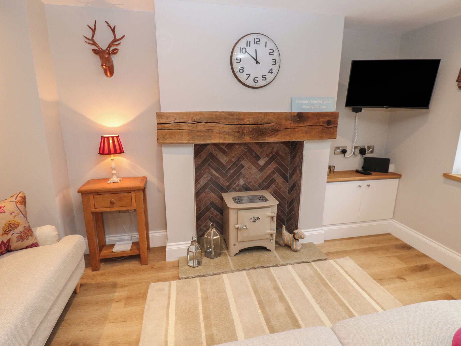 Una sala de estar con chimenea, un reloj, un televisor y una mesita con una lámpara.