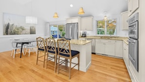 A modern kitchen with white cabinets, a central island, and pendant lighting. - Cape Cod Lake Retreat on Angus Way RPMS169 (Centerville)