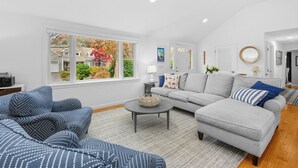 A modern living room with a grey sofa, a blue patterned sofa, and a grey armchair. There is a round coffee table in the center. - Cape Cod Lake Retreat on Angus Way RPMS169 (Centerville)