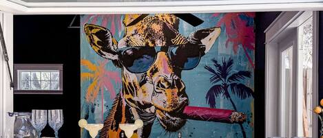 A mural of a giraffe wearing sunglasses and holding a cigar, with a tropical background.