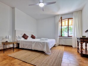 A bedroom with a bed, a bedside table, a lamp, a window with curtains, and a ceiling fan. - Apartment in a villa with a private garden, 600 meters from the beaches (San Lorenzo al Mare)