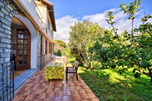 A patio with a table and chairs, a stone wall, and a garden with trees and plants. - Apartment in a villa with a private garden, 600 meters from the beaches (San Lorenzo al Mare)