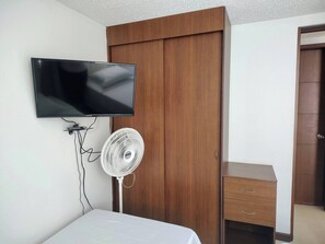 A bedroom with a bed, a TV mounted on the wall, a white fan, and a wooden wardrobe. - Comfortable Apartment in the South (Cali)