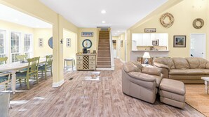 Un salón amplio con un sofá color beige, una zona de comedor con una mesa y sillas de madera, y una cocina con armarios blancos.