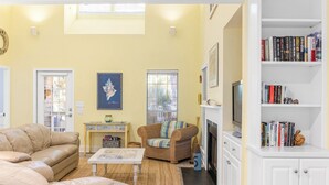 Una sala de estar con un sofá color crema, un sillón de mimbre, una mesita y una estantería llena de libros.