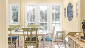 Un comedor con mesa y sillas, ventanas amplias y un adorno de pared decorativo.