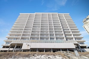 A multi-story hotel with balconies, a covered entrance, and a sign indicating a beach location. - Windemere 1404 by Liquid Life (Pensacola)