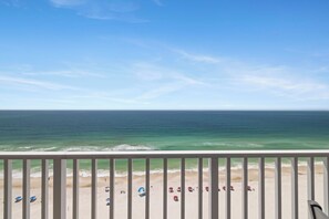 A beach view from a balcony with a railing, ocean, and beach umbrellas. - Windemere 1404 by Liquid Life (Pensacola)