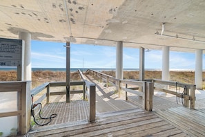 A wooden boardwalk leading to a beach with a concrete shelter overhead. - Windemere 1404 by Liquid Life (Pensacola)
