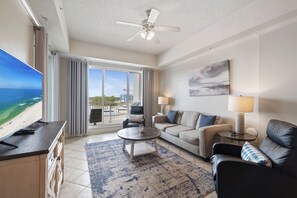 Una sala de estar moderna con televisor, sofá, mesa de centro y vistas a la playa a través de amplios ventanales.