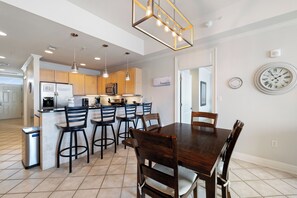 A modern kitchen with a dining area, featuring a central island, bar stools, and pendant lighting. - The Wharf 305 by Liquid Life (Orange Beach)