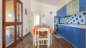 A kitchen with blue cabinets, a tiled backsplash, and a dining area with a table and chairs. - Delightful and Spacious Villa in Capo Comino (Siniscola)