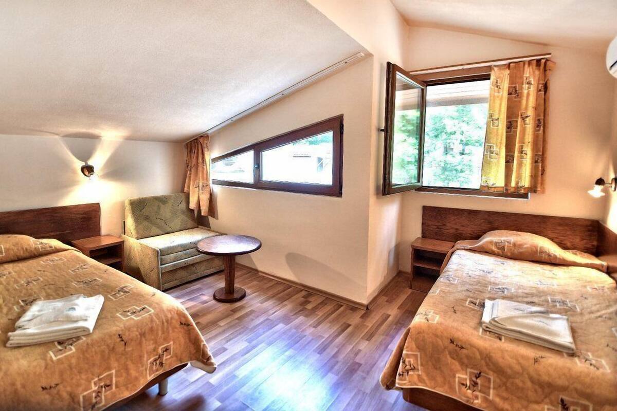 A hotel room with two beds, a small table, a chair, and a window with curtains.