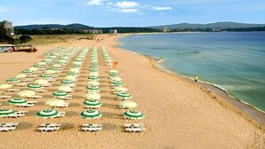 A beach with rows of sunbeds and umbrellas, a clear sky, and a calm sea. - VILLAS ROPOTAMO (Kiten)