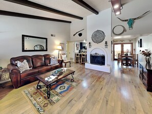 A spacious living room with a fireplace, a dining area, and a kitchen in the background. - Billy the Kid | Ground Floor, Scenic Views, & Great Location (Ruidoso)