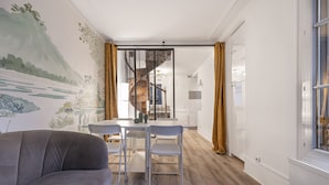 Een moderne woonkamer met een grijze bank, een eettafel met twee stoelen, en een trap die naar een verdieping leidt.