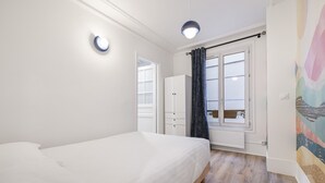 Een slaapkamer met een bed, een kledingkast, een raam met gordijnen en een plafondlamp.