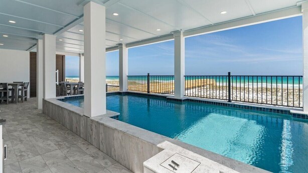 A swimming pool with a view of the beach, surrounded by white pillars and a covered area with tables and chairs. - Newly built | Luxury Gulf-front Home | Private Pool | Elevator | Game Room (Pensacola Beach)