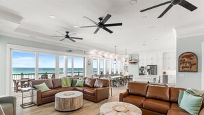 A spacious living area with a large window overlooking the ocean, a kitchen, and a dining area. - Newly built | Luxury Gulf-front Home | Private Pool | Elevator | Game Room (Pensacola Beach)