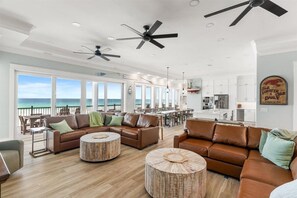 A spacious living area with a large window overlooking the ocean, a kitchen, and a dining area.