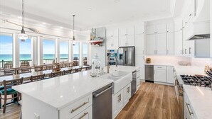 A spacious kitchen with white cabinetry, a large island, and a view of the ocean. - Newly built | Luxury Gulf-front Home | Private Pool | Elevator | Game Room (Pensacola Beach)
