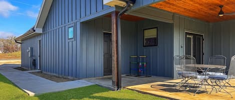 A modern house with a covered patio, a dining area with metal chairs, and a play structure.