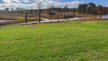 A grassy field with a small pond and a wooden structure in the distance.