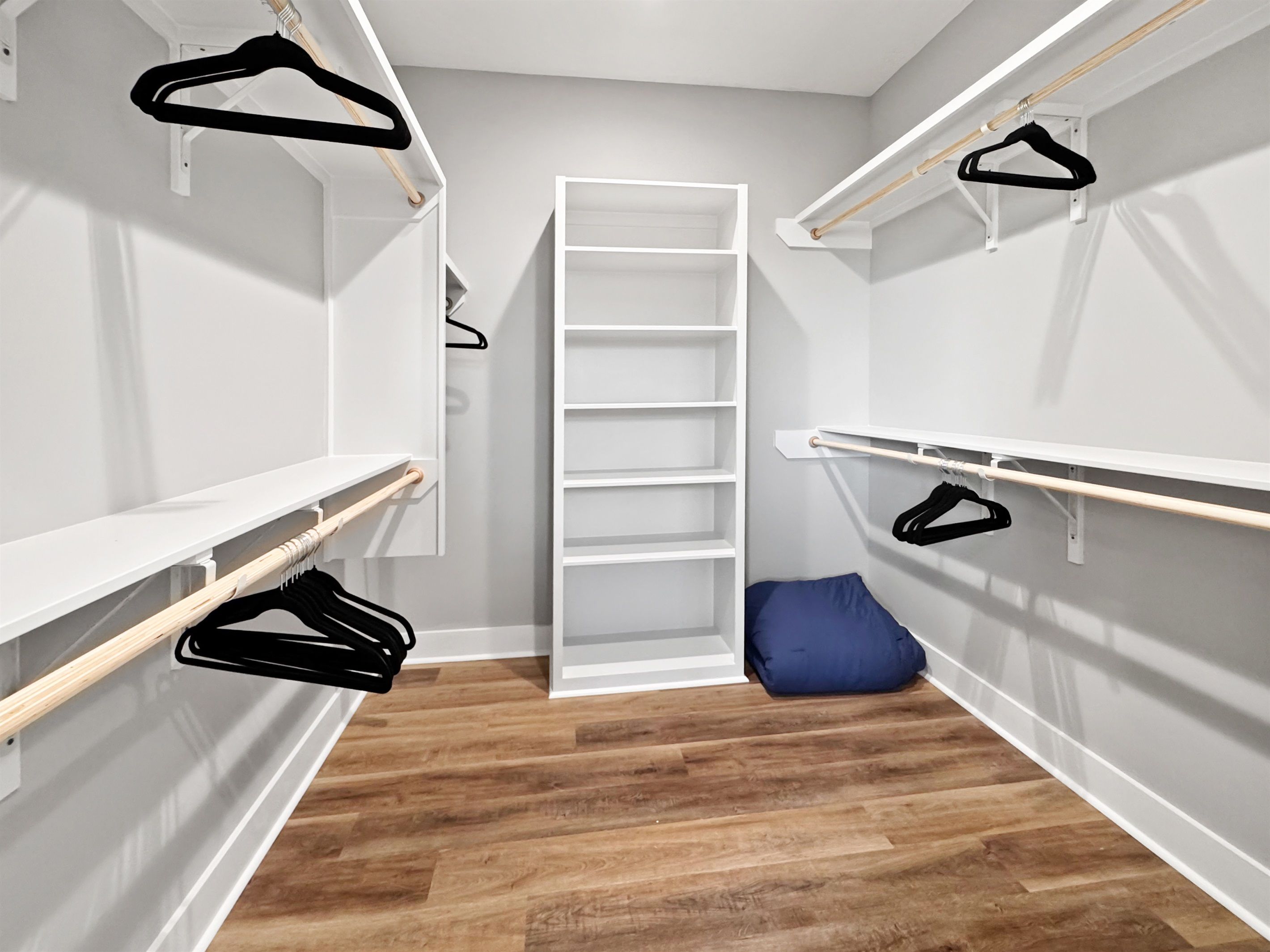 Ein begehbarer Kleiderschrank mit offenen Regalen, einer Kleiderstange und einem blauen Kissen.