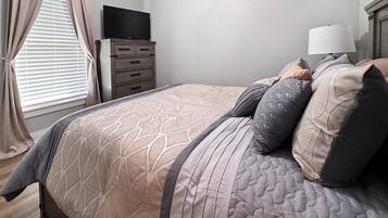 Un dormitorio con cama, cómoda, televisión y ventana con cortinas.