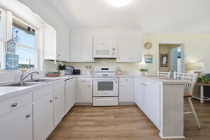 Eine Küche mit weißen Schränken, einer Mikrowelle, einem Backofen, einem Spülbecken und einem Essbereich mit Stuhl und Tisch.