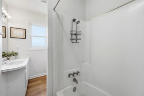 Ein Badezimmer mit weißem Waschbecken, einer Dusche mit Ablage und einem Fenster mit Blick.