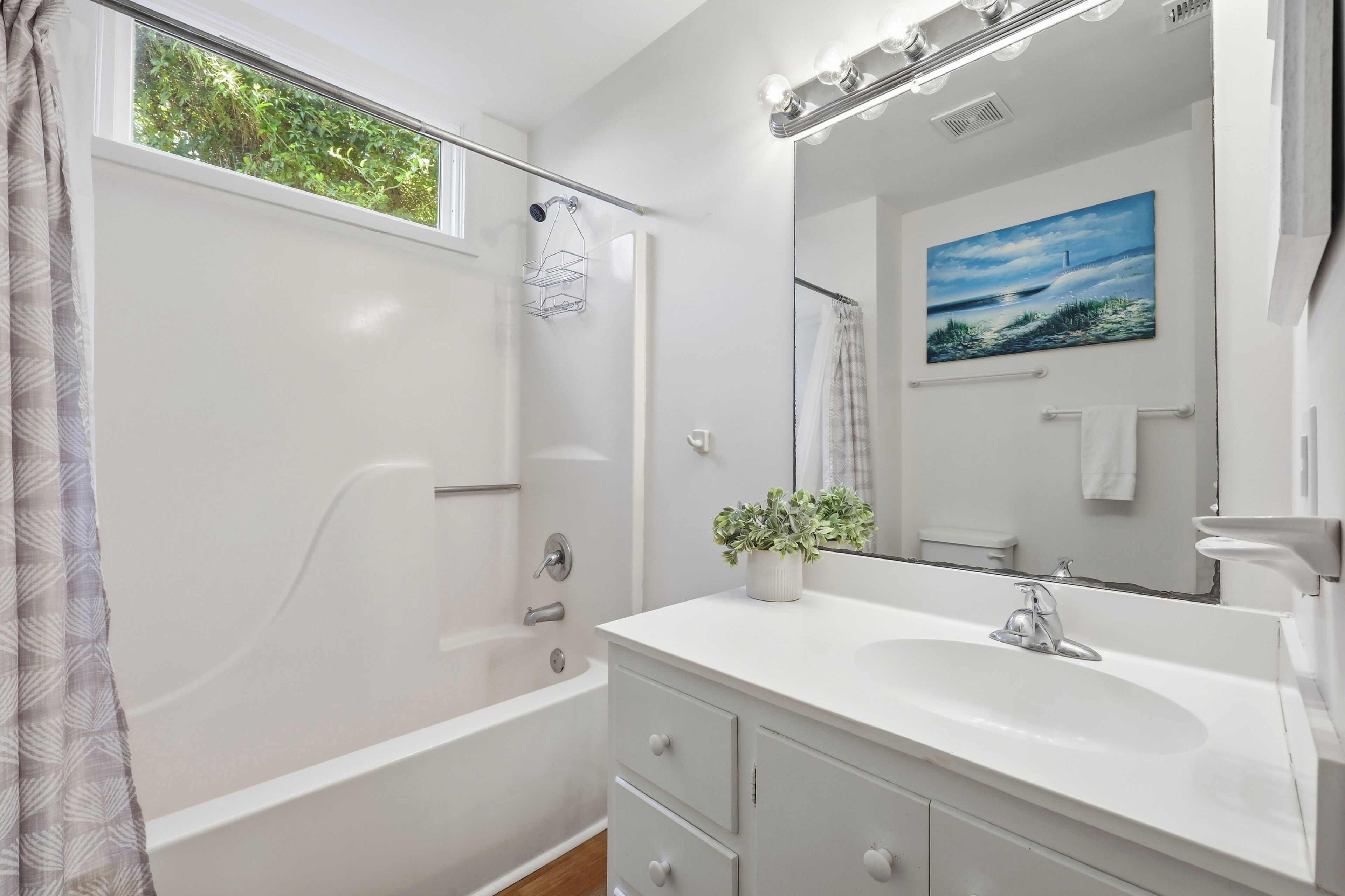 A modern bathroom with a bathtub, a sink, a mirror, and a window.